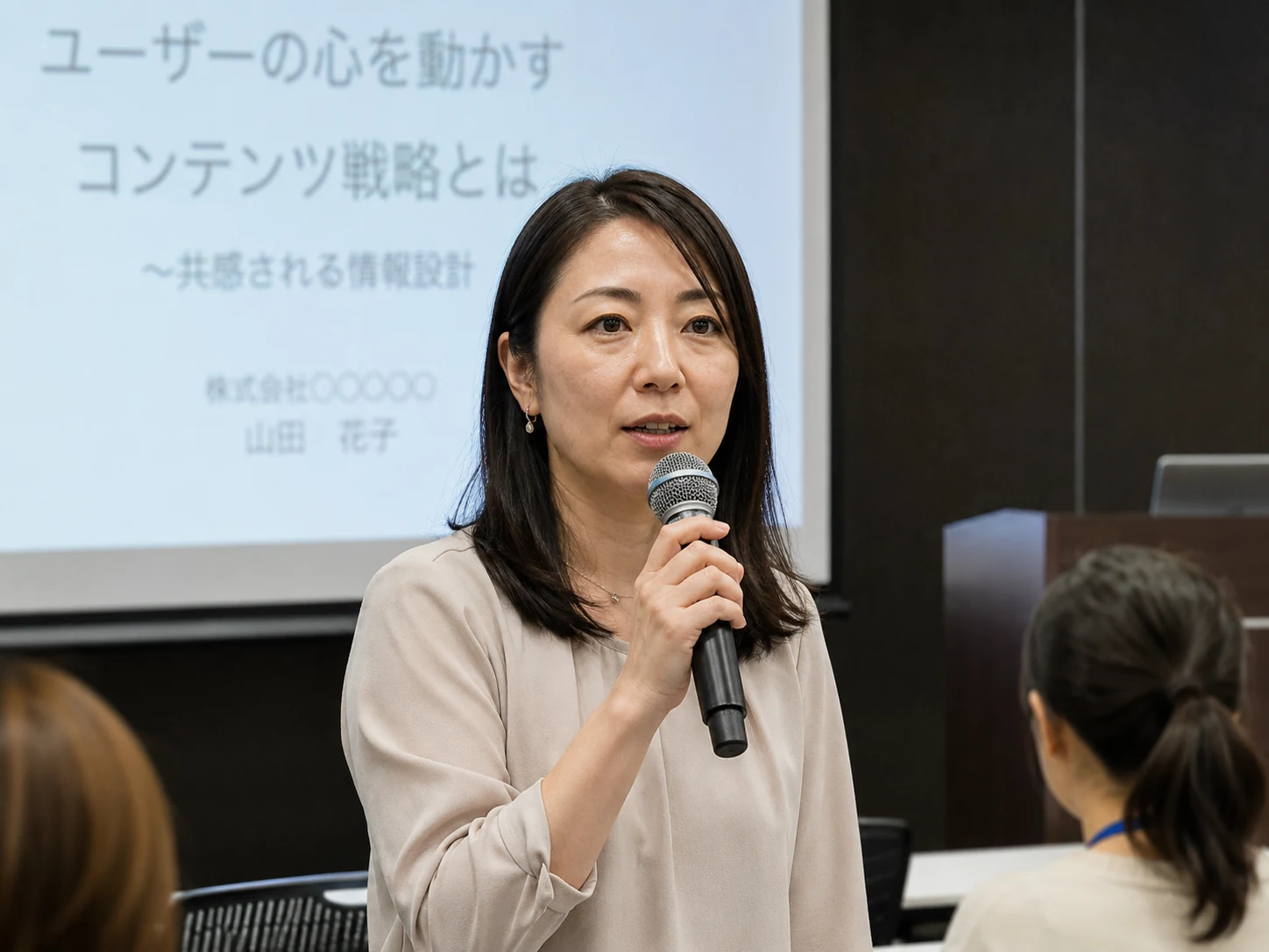 美肌補正なしの日本人女性講師が日本のセミナー会場でマイクを持って講演している様子